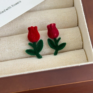 Macro shot of red velvet tulip stud earrings with green leaves in a wooden gift box