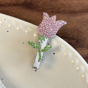 Close-up of a small tulip hair clip with pink and green rhinestones on a white plate