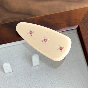 Close-up of cream teardrop hair clip with golden glitter and pink rhinestones