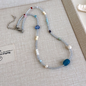 Detail der blauen Perlenkette mit weißen Perlen und silbernem Karabiner auf beigem Stoff