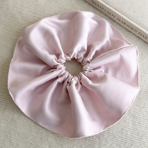 Détail d'un chouchou en satin rose clair avec une texture soyeuse sur fond beige neutre