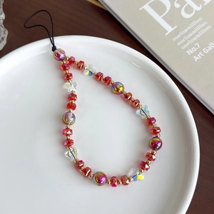 Détail de la dragonne de téléphone avec perles rouges, dorées et pendentif papillon