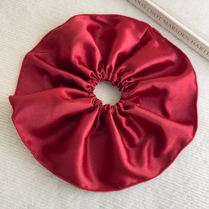 Détail d'un chouchou géant en satin bordeaux avec texture soyeuse sur fond en maille