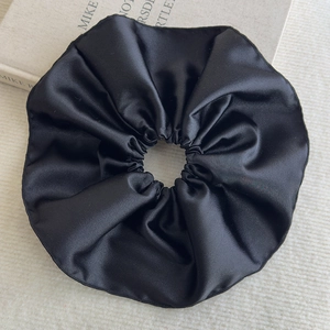 Détail d'un grand chouchou en satin noir montrant la texture soyeuse et les plis du tissu