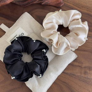 Detail of satin scrunchies in black and champagne colors with handmade pearl bead trim