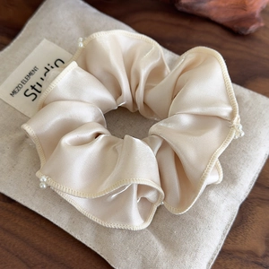 Close-up of champagne gold satin scrunchie with delicate white pearls and ruched texture