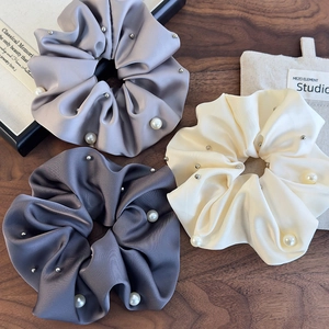 Three-piece satin scrunchies set with pearls and silver studs on dark wood background