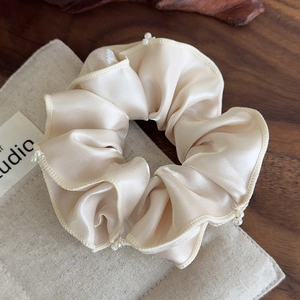 Close-up of champagne silk scrunchie with hand-sewn pearls and ruffle edges
