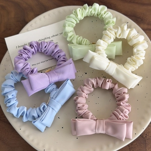 Detail showing five pastel macaron colored satin bow scrunchies on a ceramic plate