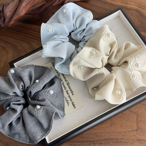 Detailed view of grey, blue and beige scrunchies with white pearls and embossed flowers