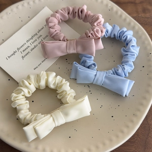 Close-up of pink, blue, and cream satin bow scrunchies on a ceramic tray display