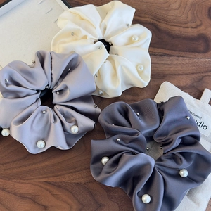 Detailed close-up of three satin scrunchies with pearls and beads on a wooden desk