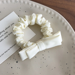 Close-up of a cream satin bow hair scrunchie placed on a ceramic plate for girls