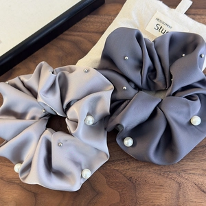 Detailed close-up of pearl and stud embellishments on satin scrunchies in gray and lilac