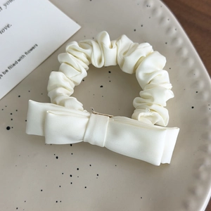 Close-up of cream bow scrunchie made of premium satin fabric on a ceramic tray