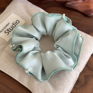 Detail view of mint green satin scrunchie with delicate ruffled edges and faux pearl accents