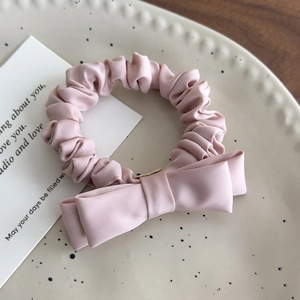Close-up of pink satin bow hair tie with ruched texture on a decorative tray