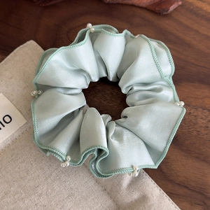 Detailed close-up of mint green satin scrunchie with delicate white pearls and wood ear edges