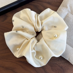 Detail of satin scrunchie featuring elegant pearls and silver studs on cream fabric