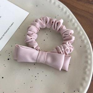 Detailed macro view of a pink bow scrunchie on a white ceramic plate with a wooden backdrop