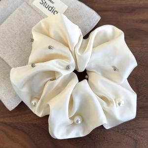 Close-up of cream satin scrunchie featuring elegant white pearls and silver metal beads