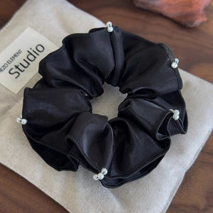 Close-up of black satin scrunchie with hand-sewn pearls and ruffle edge details