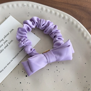 Detail view of a lavender bow hair scrunchie placed on a white polka dot ceramic plate