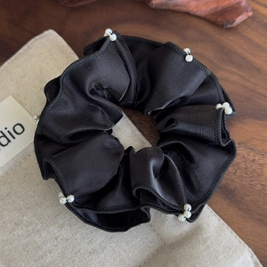 Close-up of black satin scrunchie with hand-sewn pearls and pleated ruffles on wood
