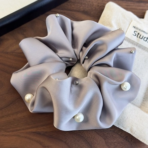 Detail of silver-grey satin scrunchie with large pearls and metallic studs on wood