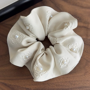 Detailed macro view of cream floral relief fabric scrunchie with faux pearl accents