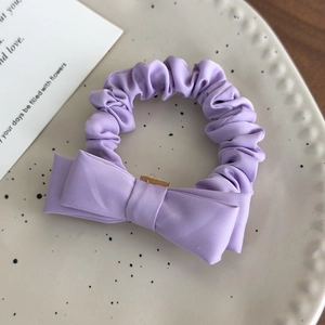 Detail of light purple bow hair scrunchie made of matte twill fabric on ceramic plate