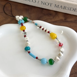 Detailed close-up of colorful mixed bead phone strap with charms on a ceramic plate