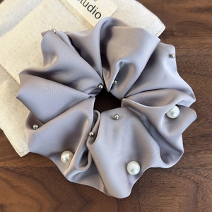 Detail view of a large light grey satin scrunchie decorated with pearls and silver studs