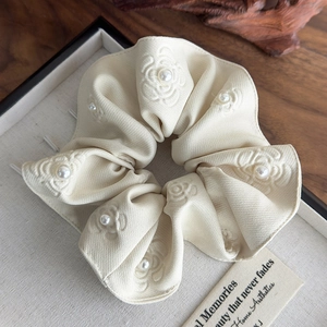 Close-up of cream fabric scrunchie with floral embroidery and elegant faux pearls