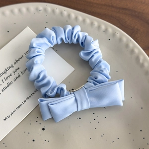 Detail of light blue satin scrunchie with double bow on a white decorative ceramic plate