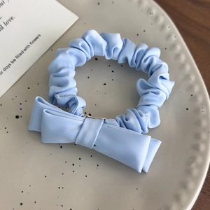 Close-up of a light blue satin scrunchie with a matching bow on a decorative cream plate