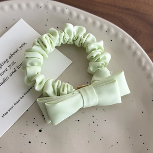 Detail of mint green satin bow scrunchie on a decorative ceramic plate with soft lighting