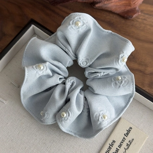 Detail of light blue floral embossed scrunchie with white pearls on a tray