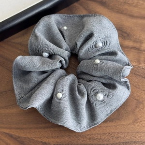 Detail of grey textured fabric scrunchie with white pearl accents on a wooden background