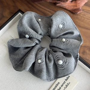 Macro shot of gray linen hair scrunchie with embedded pearls on a wooden display