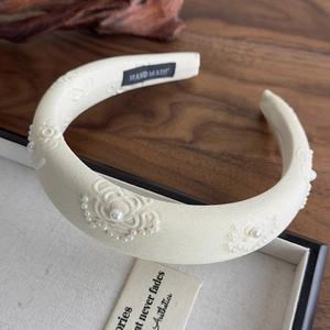 Detailed close-up of cream-white fabric headband with pearl accents and floral embroidery