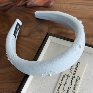 Detail view of light blue fabric headband with white pearl floral motifs and handmade label