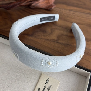 Close-up of light blue embossed fabric headband with white pearls and hand made label