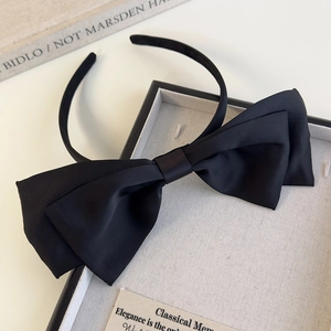 Detail shot of a layered black satin bow headband on a tray with elegant texture