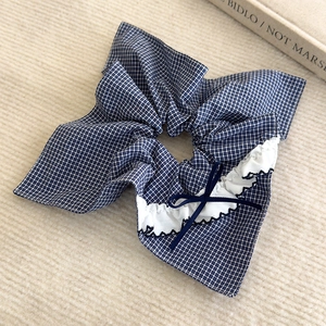 Détail d'un chouchou à carreaux bleus avec bordure en dentelle et un nœud en ruban