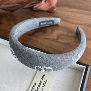 Close-up of grey fabric headband with hand-sewn pearls and black handmade woven label