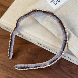 Detailed view of gray velvet headband with pearl trim on a wooden background