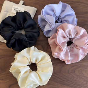 Set of four large satin scrunchies in black, lilac, pink, and cream on a wooden surface