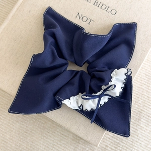 Détail d'un chouchou noeud à carreaux bleu marine avec bords en dentelle blanche