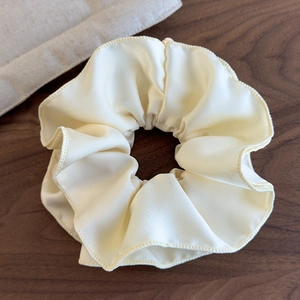 Close-up of cream yellow oversized satin scrunchie with soft pleated texture and wood decor